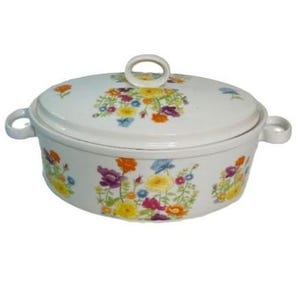 Puede incluir: Una fuente ovalada blanca con tapa, adornada con coloridos estampados florales. La fuente tiene dos asas laterales y un asa de bucle en la tapa. Las flores son en tonos amarillos, morados, naranjas y azules.