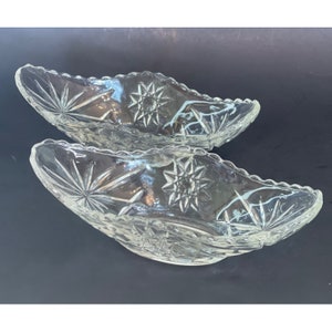 Puede incluir: Dos platos de servir de vidrio transparente con un patrón de estrella. Los platos tienen forma de media luna y tienen un borde festoneado.