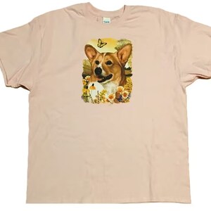 K&ouml;nnte beinhalten: Ein pinkfarbenes T-Shirt mit einem Aufdruck eines Corgi-Hundes in einem Blumenfeld mit einem Schmetterling.