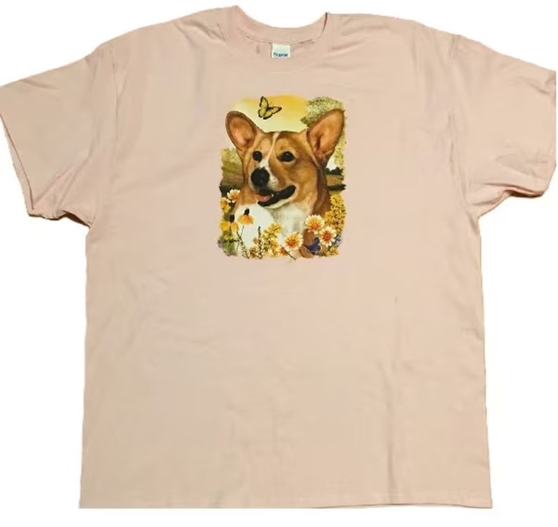 K&ouml;nnte beinhalten: Ein pinkfarbenes T-Shirt mit einem Aufdruck eines Corgi-Hundes in einem Blumenfeld mit einem Schmetterling.