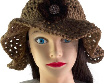 May include: A crocheted sun hat in shades of brown, featuring a dark brown flower applique and a decorative button at the center. The hat has a wide, slightly ruffled brim and an open weave design.