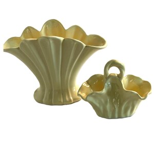 May include: A pale yellow ceramic vase with a wide, scalloped rim and vertical fluted detailing, paired with a smaller matching pale yellow ceramic basket featuring a central arched handle and a ruffled, scalloped edge design.