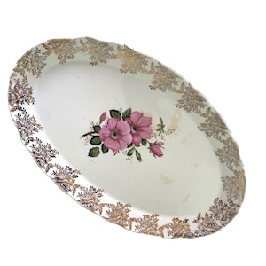 Könnte beinhalten: Ovale Servierplatte mit weißem Hintergrund, mit einem Blumendesign aus rosa Blüten und grünen Blättern. Der Rand ist mit einem gold-braunen Blumenmuster verziert. Ein Vintage-Stück zum Servieren von Speisen.