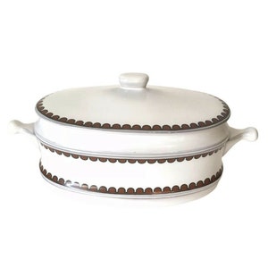 May include: White ceramic casserole dish with a lid. The dish has a brown scalloped border design and two side handles. The lid has a small knob handle. The dish is oval-shaped and appears to be new.