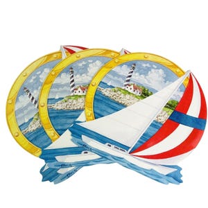May include: Set of nautical-themed decorative plates. Each plate features a lighthouse scene within a gold-colored circular frame. One plate has a sailboat with red and white stripes. The plates are stacked and overlapping.