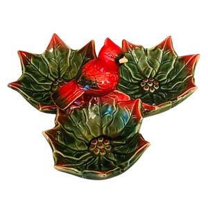 Può includere: Un set di tre piatti da portata in ceramica a forma di stella di Natale con una statuetta di cardinale rosso al centro. I piatti sono verdi e rossi con una finitura lucida.
