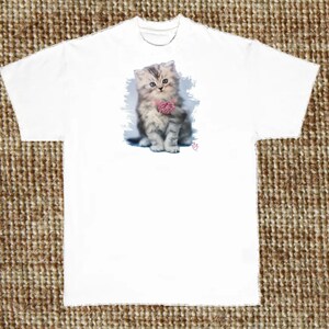 May include: A white t-shirt with a cute, gray and white kitten wearing a pink bow. The kitten is sitting on a blue and white background.
