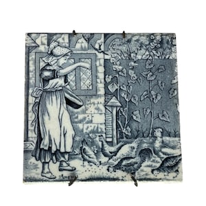 May include: A blue and white ceramic tile depicting a woman in a long dress and bonnet feeding chickens in a garden. The tile is labelled "August" in the bottom right corner.