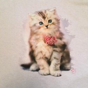 May include: A white and gray kitten with blue eyes is sitting on a light purple background. The kitten is holding a pink flower in its paws. The image has a pink heart with a paw print in the bottom right corner.