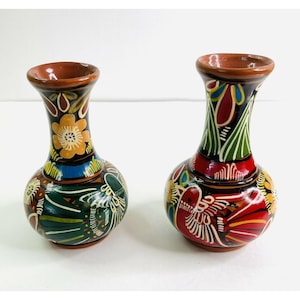 May include: Two small, hand-painted ceramic vases. The vases have a bulbous base and a narrow neck, with a brown rim. The colorful designs include flowers, birds, and geometric patterns in red, yellow, green, and blue.