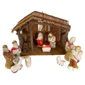 May include: A vintage Christmas nativity scene with a rustic wooden stable and figurines. The stable has a thatched roof and a wooden frame. The figurines include Mary, Joseph, baby Jesus, shepherds, and animals. The figures are painted in various colors.