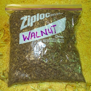 May include: A clear plastic bag with a Ziploc brand label and the word "WALNUT" written on it in purple marker. The bag contains a large amount of finely chopped walnut wood.