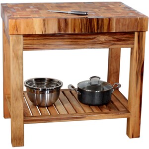 May include: A wooden kitchen island with a butcher block countertop and a lower shelf. The island is made of natural wood with a light brown finish. The countertop has a checkered pattern and is made of different types of wood. The lower shelf is made of slats of wood and is empty.