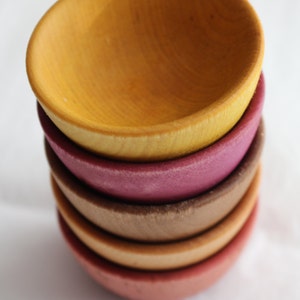 May include: A stack of four wooden bowls in different colors. The top bowl is yellow, the second is purple, the third is brown, and the bottom bowl is orange.