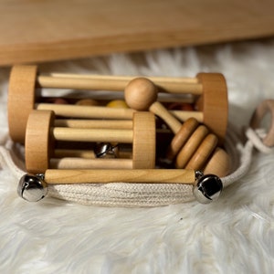 Four handmade musical montessori materials made from birch hardwoods resting in a handmade rope basket on top of a white furry play mat and wood shelf behind.