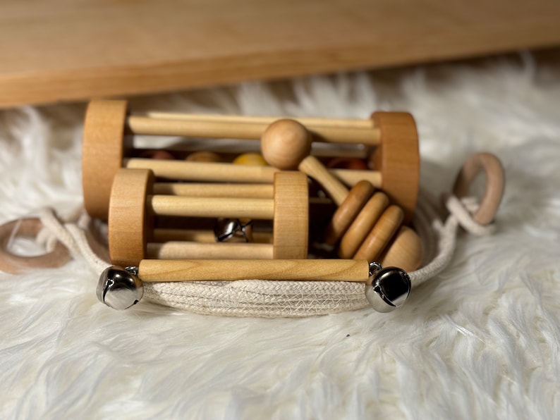 Four handmade musical montessori materials made from birch hardwoods resting in a handmade rope basket on top of a white furry play mat and wood shelf behind.