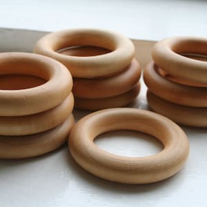 May include: A stack of five wooden rings, each with a smooth, natural finish. The rings are arranged in a pyramid shape, with the largest ring at the bottom and the smallest ring at the top.