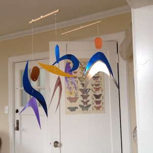 May include: A mobile made of colorful geometric shapes hangs from the ceiling. The shapes are made of metal and are suspended by strings. The mobile is a modern and abstract design.