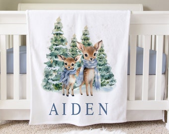 May include: White baby blanket featuring a watercolour illustration of two deer wearing blue scarves in front of a snowy woodland scene. The blanket has the name "AIDEN" printed in blue at the bottom.