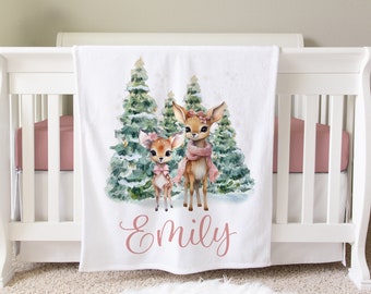 May include: White baby blanket with a pink personalised name "Emily" and a watercolour illustration of two deer in a snowy forest with pine trees.