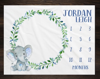 May include: A white baby milestone blanket with a blue and green leafy wreath and a cute gray elephant. The blanket has numbers 1-12 for each month and the text "JORDAN LEIGH" and "MONTHS".