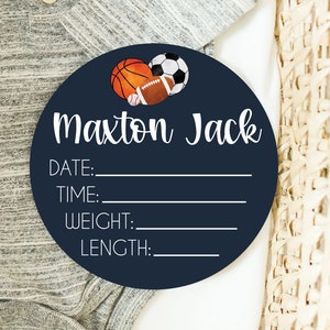 以下が含まれることがあります： 白枠と白文字で縁取られた濃い青色の丸い木製看板。看板には、バスケットボール、アメリカンフットボール、サッカーボールの水彩画が描かれている。看板の文字は「Maxon Jack」、「日付:」、「時間:」、「体重:」、「長さ:」。