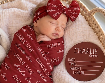 Könnte beinhalten: Ein Neugeborenes, eingewickelt in eine dunkelrote Decke mit dem wiederholten weißen Text "CHARLIE LOVE", trägt ein passendes Schleifen-Stirnband. Eine runde dunkelrote Holzplakette mit dem weißen Text "CHARLIE LOVE" und leeren Zeilen für Geburtsdaten.