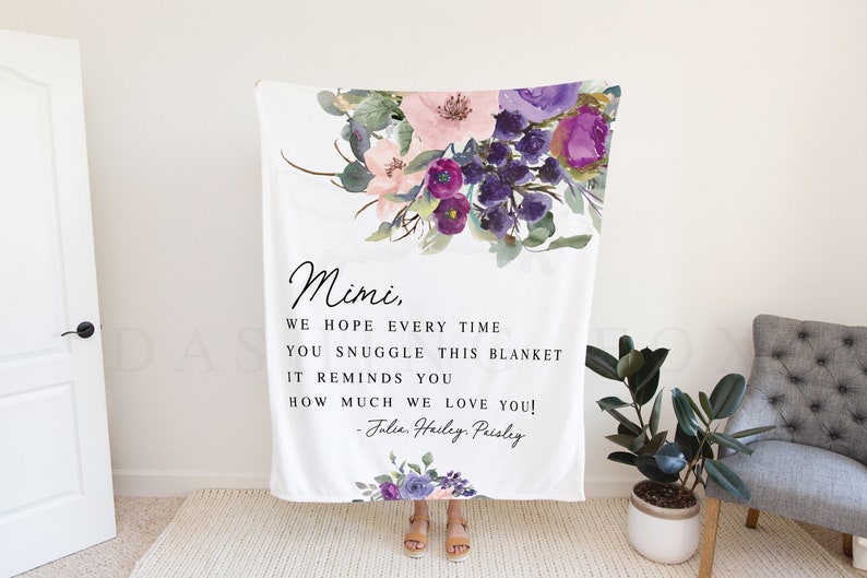 Puede incluir: Una manta blanca con un dise&ntilde;o floral en tonos de morado, rosa y verde. La manta tiene un mensaje personalizado que dice: "Mimi, Esperamos que cada vez que te acurruques en esta manta, te recuerde cu&aacute;nto te queremos! - Jalie Hailey Peisley".