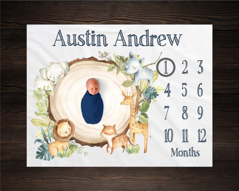 K&ouml;nnte beinhalten: Eine wei&szlig;e Babydecke mit einer Aquarell-Illustration eines Baumstumpfes, der von Tieren umgeben ist. Das Baby liegt auf der Decke, und der Text "Austin Andrew" befindet sich oben auf der Decke. Die Zahlen 1 bis 12 sind auf der rechten Seite der Decke aufgelistet, mit dem Wort "Monate" unter den Zahlen.