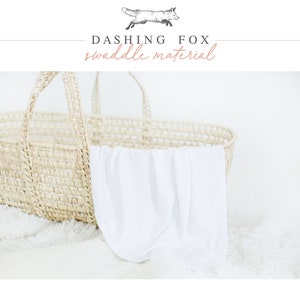 Puede incluir: Una cesta tejida con asas contiene una manta blanca para envolver al beb&eacute;. El texto "Dashing Fox swaddle material" est&aacute; encima de la cesta, con un dibujo de un zorro. La cesta est&aacute; sobre una superficie blanca y esponjosa.