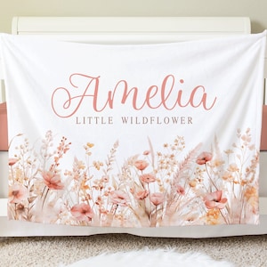Puede incluir: Una manta de bebé blanca con un diseño floral rosa y el texto "Amelia Little Wildflower".