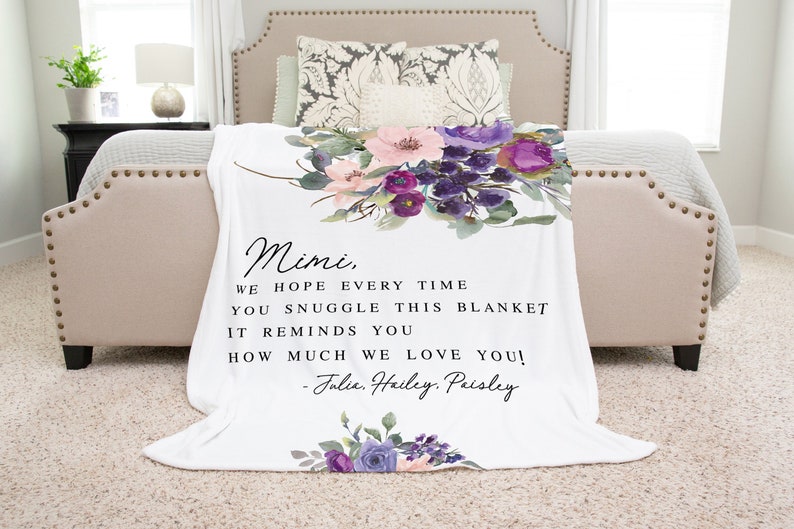 Puede incluir: Una manta blanca con un dise&ntilde;o floral en tonos de morado, rosa y verde. La manta tiene un mensaje personalizado que dice: "Mimi, Esperamos que cada vez que te acurruques en esta manta, te recuerde cu&aacute;nto te queremos! -Julia. Hailey. Paisley"