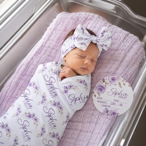 May include: A white swaddle blanket and matching headband featuring a purple floral pattern and the name Sophia Violet printed in black script. A circular white sign with matching floral graphics and the name Sophia Violet with blank lines.
