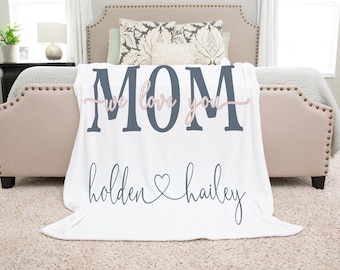 Może przedstawiać: Biały koc z polaru z napisem "MOM we love you" w kolorze granatowym i "holden hailey" w kolorze granatowym z różowym sercem między imionami.