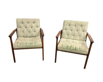 May include: Two vintage armchairs with light green tufted upholstery and wooden frames. The cushions show signs of wear. The armrests and legs are a dark wood. The chairs are set against a white background.
