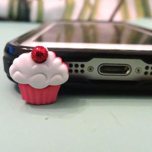 May include: A red and white cupcake phone charm with a red glitter cherry on top.