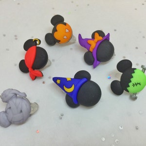 May include: Six Halloween-themed character charms featuring Mickey Mouse in various costumes. The charms are made of black, green, purple, orange, and gray plastic. The characters include a pirate, a witch, a Frankenstein, a mummy, and two Mickey Mouse characters.