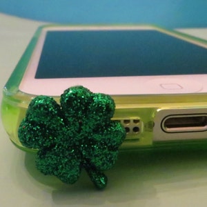 May include: A green glitter shamrock charm attached to a clear phone case.