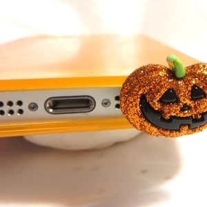 May include: Orange glitter pumpkin phone charm with a black jack-o'-lantern face and a green stem.