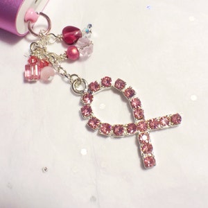 May include: A pink rhinestone charm in the shape of a ribbon, attached to a silver chain with pink and clear beads.