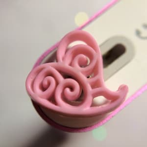 May include: A pink heart-shaped charm with a swirling design. The charm is made of plastic and has a glossy finish.