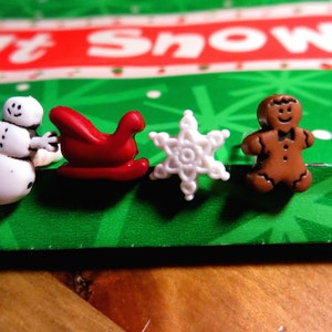 May include: Four Christmas-themed buttons: a white snowman, a red sleigh, a white snowflake, and a brown gingerbread man.