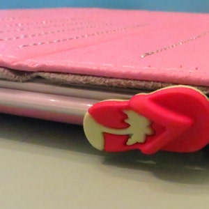 May include: A pink leather case with a red and white flip-flop charm attached to the side.