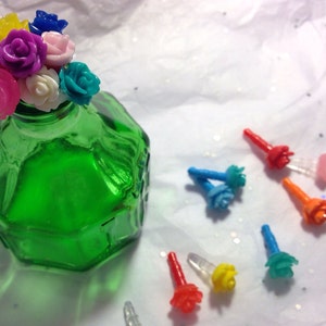 May include: A collection of colorful plastic flower bottle stoppers. The stoppers are in various colors, including pink, blue, yellow, and green. The stoppers are arranged in a bouquet shape and are sitting on top of a green glass bottle.