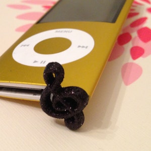 May include: A gold iPod with a black treble clef charm attached to the bottom. The iPod has a black and white screen and a circular button with the word "MENU" printed on it.
