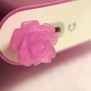 May include: A pink plastic rose flower charm, attached to a pink electronic device.