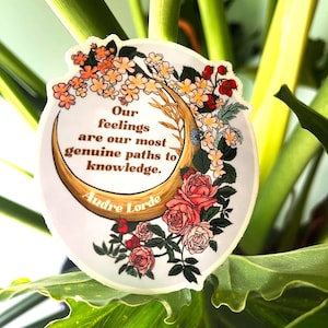 May include: A white sticker with a crescent moon and floral design. The text on the sticker reads "Our feelings are our most genuine paths to knowledge. Audre Lorde."