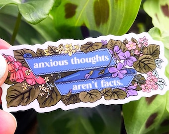 Könnte beinhalten: Ein Aufkleber mit einem floralen Rand und einem blauen Band mit dem Text "anxious thoughts aren't facts".