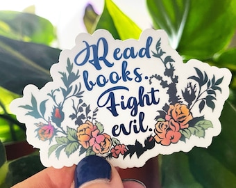 May include: A white sticker with a floral wreath design. The text "Read books. Fight evil." is written in blue inside the wreath.