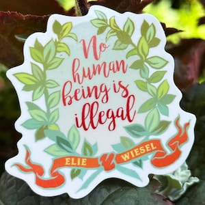 Può includere: Un adesivo con la scritta "No human being is illegal" in rosso, circondato da una ghirlanda di foglie verdi. L'adesivo presenta anche uno striscione con il nome "Elie Wiesel" in arancione.